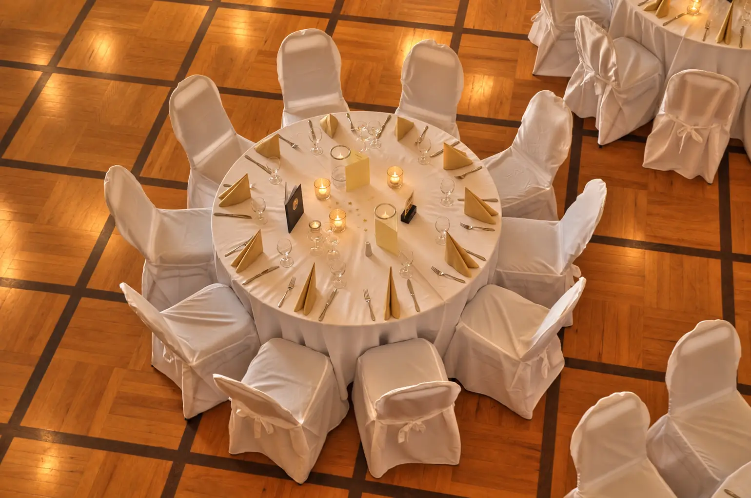 Festlich gedeckter runder Tisch mit Gläsern, Blumenschmuck und weißen Stühlen im Ballsaal